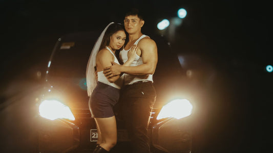 Couple embracing in front of a parked car at night, headlights glowing — a private romantic moment