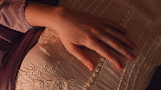 Close-up of a woman's hand resting on lace lingerie and a satin robe — sensual self-touch