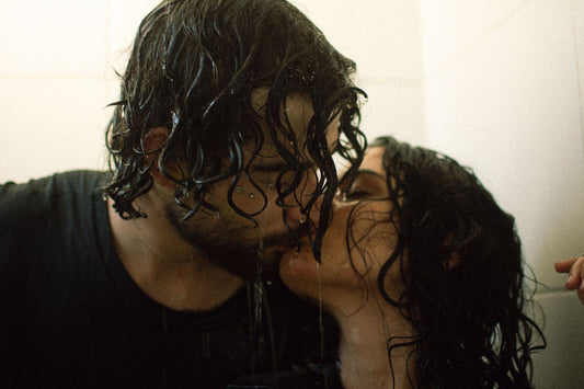 Couple with wet hair kissing closely under a warm shower in a steamy, romantic moment
