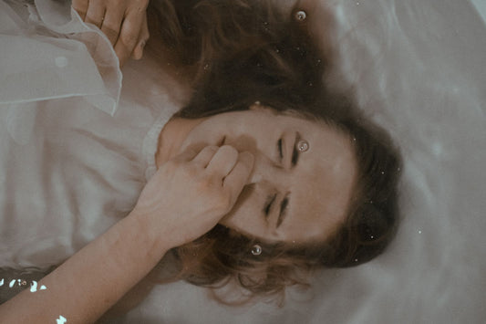 Woman lying back on soft white sheets, laughing and relaxed in warm light