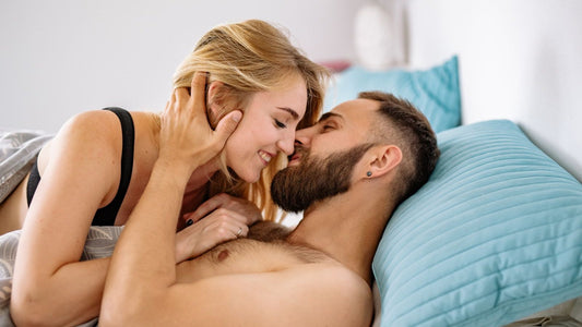 Couple kissing in bed, woman cradling her partner's face — slow, connected intimacy
