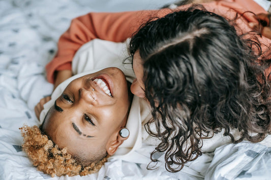 Two women laughing in a joyful intimate embrace on a bed, tasteful romantic connection