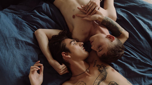 Two men lying together in bed, relaxed and close — male intimacy and pleasure
