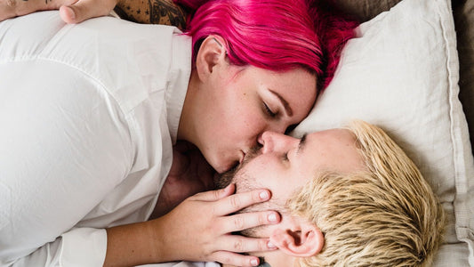 Partner kissing a woman who lies back relaxed on the pillows — receptive, pampered intimacy