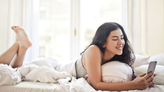 Smiling woman lying on her bed texting on her phone — playful app-controlled flirting