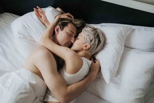 Couple embracing closely in white bed sheets, faces together in a slow, intimate moment