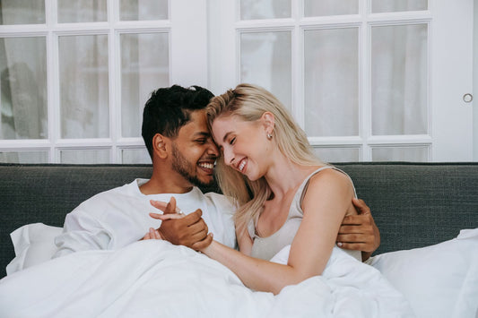 Couple snuggling forehead to forehead in bed, smiling and holding hands